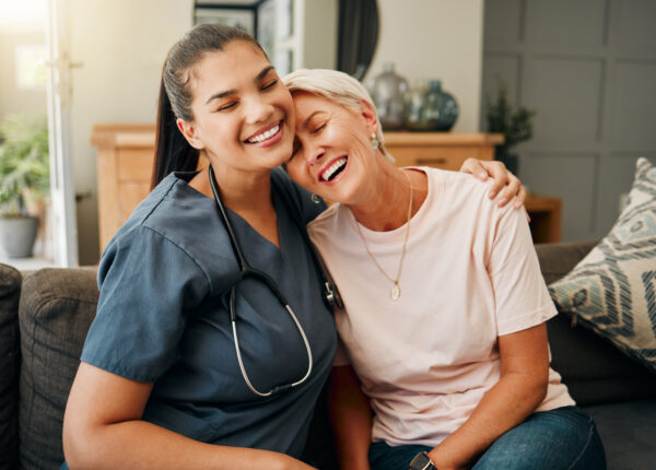 Senior woman, hug or medical caregiver in house living room in comfort trust, support or security bond. Smile, happy or laughing nursing home retirement elderly and healthcare Brazilian nurse or help.