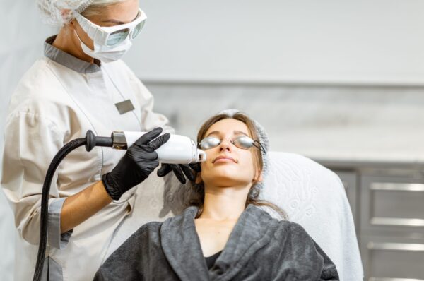 Professional doctor in protective wear making a laser rejuvenation treatment for a young woman client at medical office. LaseMD procedure