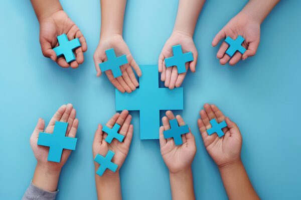 hands holding a red plus sign on a blue background, taken from a top view. The concept represents World Health Day and medical care concepts. A banner with copy space text.