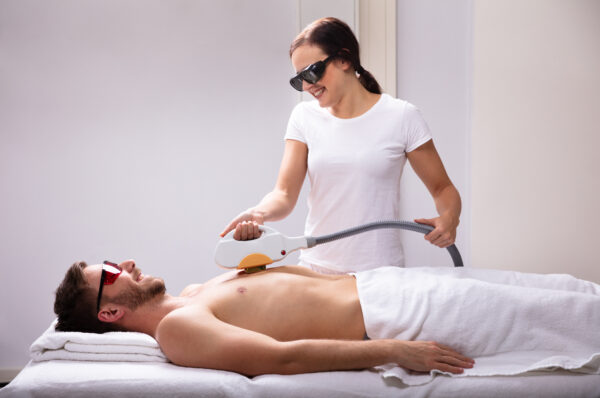 Young Female Beautician Giving Laser Depilation Treatment On Relaxed Man's Chest