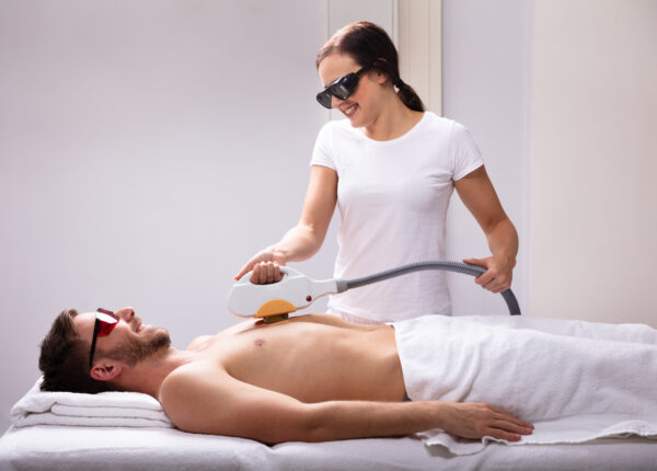 Young Female Beautician Giving Laser Depilation Treatment On Relaxed Man's Chest