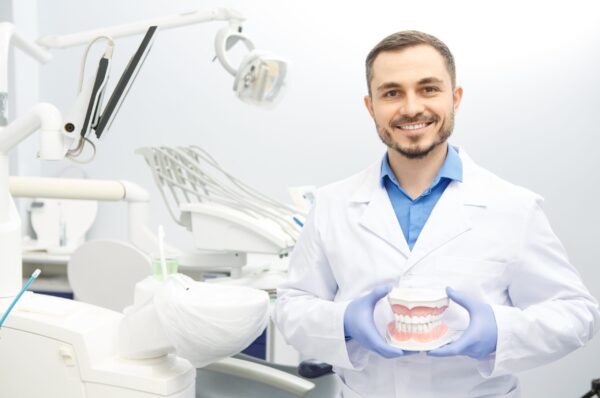 Mature male dentist smiling cheerfully to the camera holding dental mold posing at his office copyspace dentistry stomatology medicine health jaw model confidence professionalism care concept