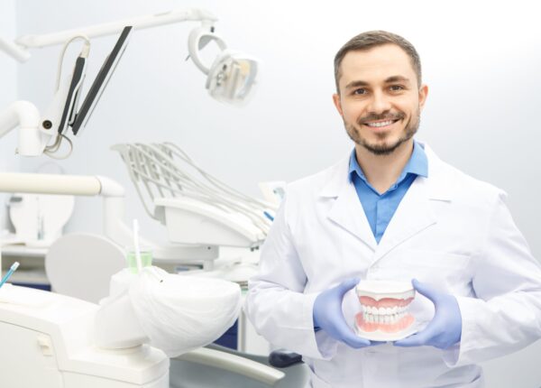 Mature male dentist smiling cheerfully to the camera holding dental mold posing at his office copyspace dentistry stomatology medicine health jaw model confidence professionalism care concept