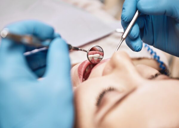 Close-up of woman opening her mouth wide during inspection of oral cavity. Dentist is checking up her teeth using dental tools. Medicine and health care concept. Focus on dental tools. Horizontal shot